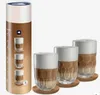 A cylindrical product packaging and three glasses filled with coffee and foam are displayed against a white background. Anteprima dell’immagine prodotto