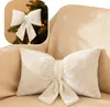 A cream-colored bow-shaped pillow is placed on a cream-colored sofa. A smaller inset image shows a similar bow on a Christmas tree. Podgląd zdjęcia produktu