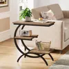 A narrow C-shaped side table with three shelves is placed next to a sofa in a living room. Voir les images du produit