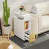 A white side table with a drawer and shelves is placed next to a cream-colored sofa. A tall cactus plant in a white pot stands to the left of the table. Books and a small vase of flowers are on top of the table. Voir les images du produit