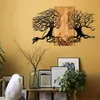 A wall art piece depicting two tree-like faces facing each other, mounted on a wooden panel, displayed on a yellow wall above a shelf with decorative items. Produktbild-Vorschau