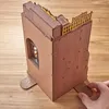 A hand is shown inserting a piece into a 3D wooden puzzle book nook. Náhled obrázku produktu