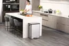 A woman is washing vegetables in a modern kitchen island, with a stainless steel trash can next to it. Voir les images du produit