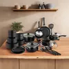 A collection of black cookware and dinnerware is arranged on a wooden table, with a shelf holding decorative items in the background. Produktbild-Vorschau