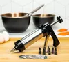A cookie press with various attachments and accessories, along with baking ingredients like eggs and bowls, is displayed on a wooden surface. Podgląd zdjęcia produktu