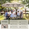 A group of people are gathered around a table outdoors, under a large beige umbrella. Náhled obrázku produktu