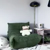 A green sofa with a teddy bear on it, next to a floor lamp and a side table. Voir les images du produit