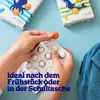 Hands holding a blister pack of orange gummy bears, with two boxes of the product in the background and a blue towel on the right. Produktbild-Vorschau