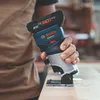 A person is holding a Bosch cordless router and using it on a wooden surface. Voir les images du produit