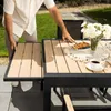 A person is extending a table leaf on an outdoor dining table set with food and drinks. Produktbild-Vorschau