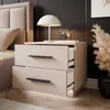 A modern bedside table with two drawers, a lamp, and decorative items on top, placed next to a bed. Produktbild-Vorschau