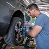 A man is using a Bosch cordless impact wrench to tighten the lug nuts on a car wheel, which is elevated on a lift. Voir les images du produit