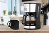 A coffee maker and two mugs are on a wooden table in a kitchen setting. Produktbild-Vorschau