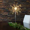 A starburst LED light decoration is placed on a table with a garland of greenery and pinecones. Produktbild-Vorschau