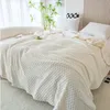 A white textured blanket draped over a bed with pillows. Náhled obrázku produktu