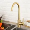 A gold kitchen faucet is shown in a kitchen sink area, with some vegetables in a rack nearby. Produktbild-Vorschau