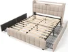 A beige upholstered bed frame with wooden slats and drawers pulled out, shown from a diagonal angle against a white background. Náhled obrázku produktu