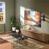 A living room with a TV mounted on the wall above a media console, with plants and a coffee table in the foreground. Produktbild-Vorschau
