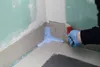 A person is applying a grey waterproofing compound to the corner of a bathroom wall and floor. Produktbild-Vorschau