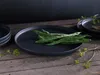 A dark grey plate with green beans on top, set on a wooden table with some greenery. Náhľad obrázku produktu