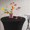A black tablecloth-covered round table with floral arrangements and decorative objects against a tiled wall. Produktbild-Vorschau
