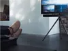 A person's feet are resting on a table in front of a TV on a tripod stand. Anteprima dell’immagine prodotto