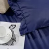 A close-up of a navy blue duvet cover with a ruffled edge, placed over a magazine featuring a woman's portrait and a white teacup and saucer. Produktbild-Vorschau