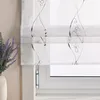 A close-up view of a white sheer Roman blind with a gray embroidered swirl pattern, partially covering a window. A vase with lavender is visible on the left. Produktbild-Vorschau