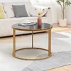 A round coffee table with a marble top and gold legs is placed on a rug in front of a sofa. A vase with dried flowers and a cup of coffee are on the table. Produktbild-Vorschau