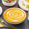 A close-up shot of a bowl of orange soup with a decorative swirl of cream, placed on a table with cutlery and other dishes. Produktbild-Vorschau