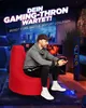 A man is playing a video game while sitting on a red beanbag chair in a dimly lit room. Produktbild-Vorschau
