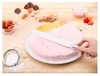 A hand is using a spatula to spread pink frosting on a cake, with strawberries, chocolate, and powdered sugar scattered around. Produktbild-Vorschau