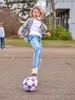 A young girl is playing with a soccer ball on an outdoor paved area. Anteprima dell’immagine prodotto