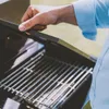 A person's hand is opening the lid of a black gas grill. Náhľad obrázku produktu