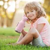 A young child sitting in the grass and holding a pink water bottle. Anteprima dell’immagine prodotto