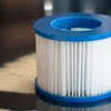 A close-up shot of a white pleated pool filter with blue plastic rims, resting on a reflective dark surface. Produktbild-Vorschau