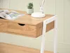 A close-up view of a wooden desk with white metal legs, showing a drawer, a magazine, a plant, and a lamp. Voir les images du produit