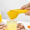 A person is squeezing juice from a lemon into a glass using a yellow citrus squeezer. Produktbild-Vorschau
