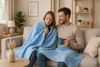 A couple is sitting on a sofa, sharing a blanket and a mug. Produktbild-Vorschau