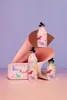 A collection of pink water bottles and a lunchbox with a unicorn and rainbow pattern, arranged on a pink surface with a purple background and brown and pink paper elements. Produktbild-Vorschau