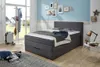 A bedroom scene with a bed, coat rack, suitcase, and decorative items. Produktbild-Vorschau