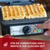 A waffle maker with two waffles inside, a hand pressing a button, and text overlay. Produktbild-Vorschau