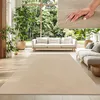 A living room scene with a large beige rug, sofas, plants, and a large window overlooking a garden.