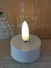 A close-up shot of a white LED tea light with a flickering yellow flame, set against a rustic wooden background. Produktbild-Vorschau