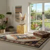 A living room scene with a decorative wooden cube stand, a rug, plants, and a large window overlooking a garden. Produktbild-Vorschau
