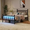 A bedroom scene featuring a black metal bed frame with LED lighting underneath, dressed with bedding and pillows. Storage boxes are placed beneath the bed. Produktbild-Vorschau