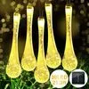 A string of solar-powered teardrop-shaped lights hanging in a garden setting. Produktbild-Vorschau