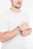 A man wearing a white t-shirt is shown from the chest up, with his left arm crossed over his chest and his right hand resting on his left arm. He is wearing a gold digital watch on his left wrist. Podgląd zdjęcia produktu