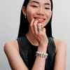 A woman wearing jewelry, including a bracelet with charms and a ring. Voir les images du produit