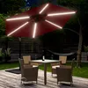 An outdoor patio scene at night with a red cantilever umbrella illuminated by LED lights, a table with chairs, and a hammock in the background. Produktbild-Vorschau
